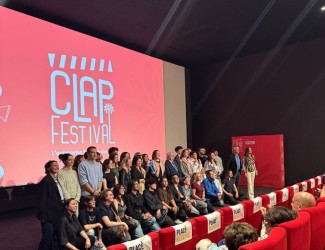 Groupe de participants posant sur scène devant un écran affichant “CLAP Festival”, dans une salle de cinéma avec des sièges rouges au premier plan.