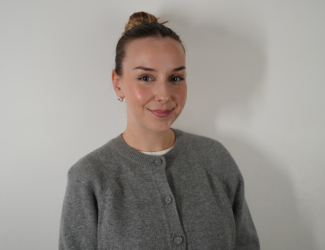Portrait d’une jeune femme souriante, cheveux attachés, portant un haut gris sur fond clair