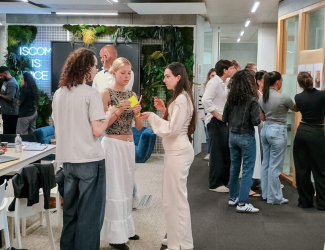 Des étudiants échangent en petits groupes dans un espace de travail moderne et convivial, avec des post-it en main et un mur végétalisé en arrière-plan.