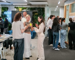 Des étudiants échangent en petits groupes dans un espace de travail moderne et convivial, avec des post-it en main et un mur végétalisé en arrière-plan.