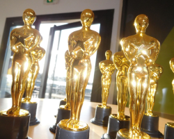 Plusieurs statuettes dorées ressemblant aux trophées des Oscars sont disposées sur une table. La lumière du soleil brille à travers une porte vitrée en arrière-plan, produisant des reflets sur les trophées.